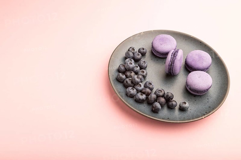 Purple macarons or macaroons cakes with blueberries on ceramic plate on a pastel pink background. Side view, close up, copy space