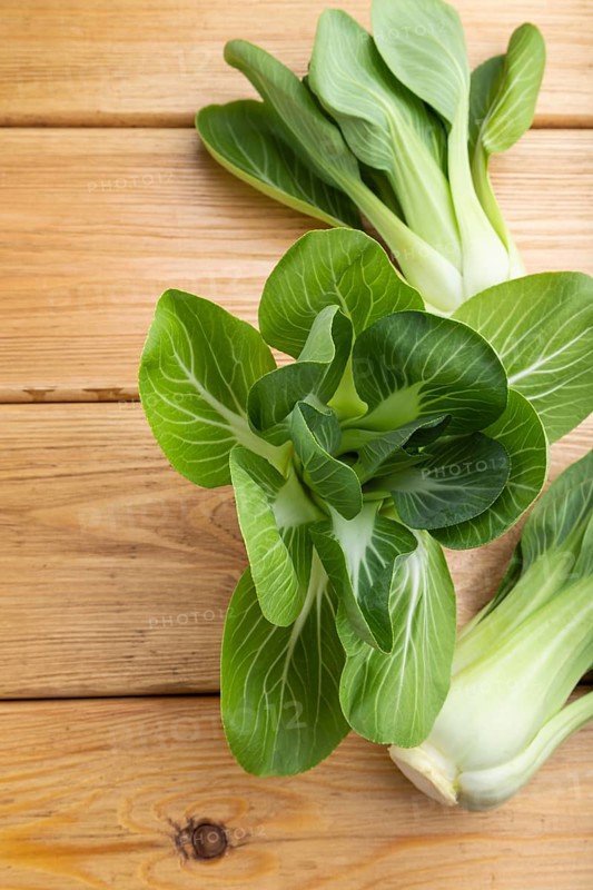 Fresh green bok choy or pac choi chinese cabbage on a brown wooden background. Top view, close up, flat lay