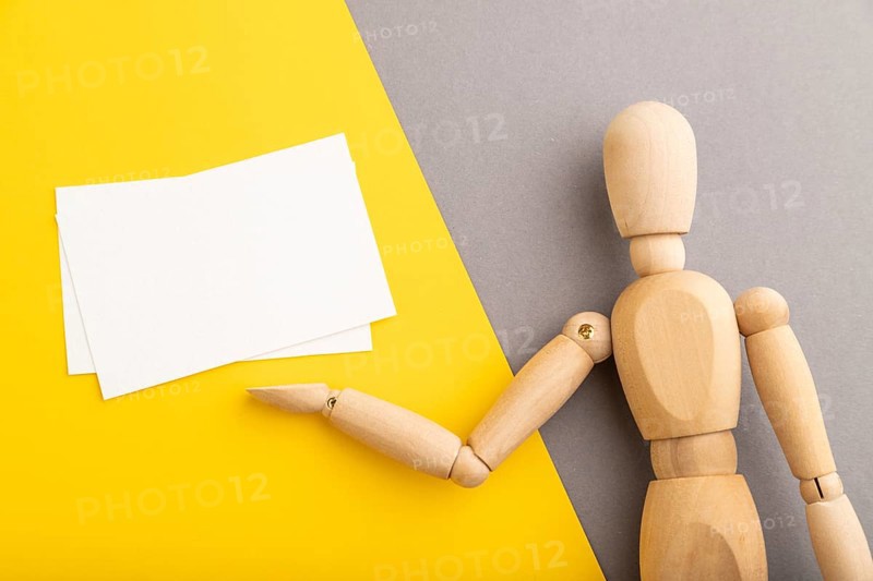 Wooden mannequin holding white blank poster on gray and yellow pastel background. copy space, isolated, presentation concept, trendy colors