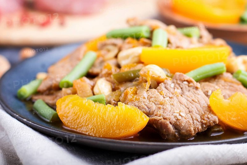 Fried pork with peaches, cashew and green beans on a black concrete background. Side view, close up, chinese cuisine, selective focus, macro