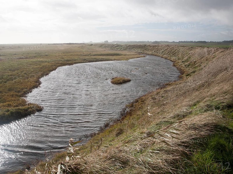 Marshland behind vegetated shingle with lagoon water bounded by costal defence sea wall, Alderton, Suffolk, England, UK