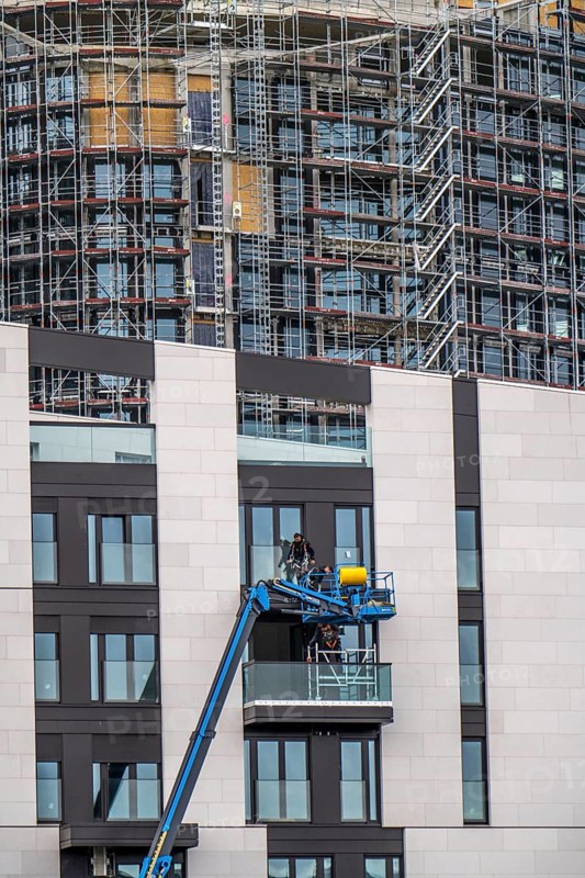 Large construction site, construction of a high-rise residential building, scaffolded shell, already fitted with windows, finished building in front, facade work with a cherry picker
