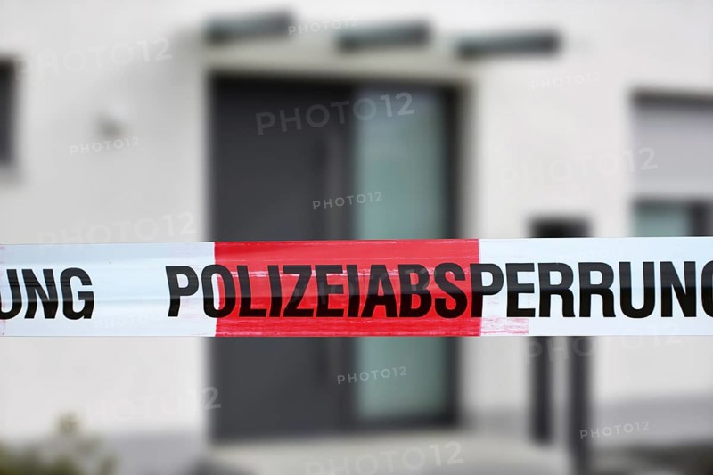 Symbolic image: Barrier tape with the inscription police cordon, in the background a residential building (Composing)