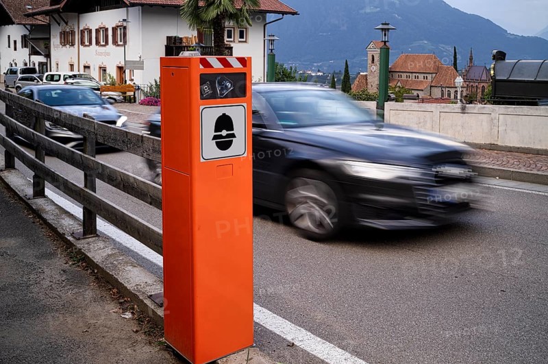 Fake speed camera with stick-on camera, fake speed camera, radar, dummy, speed measurement, speeding, car, movement, wiping effect, speed, behind it new parish church Maria Himmelfahrt, traffic, Schenna, Scena, South Tyrol, Autonomous Province of Bolzano, Italy, Europe