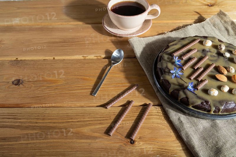 Homemade chocolate brownie cake with caramel cream and almonds with cup of coffee on wooden background and linen textile. Side view, hard light, copy space