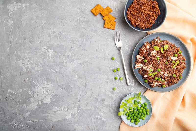 Quinoa porridge with green pea and chicken on ceramic plate on a gray concrete background and orange textile. Top view, flat lay, copy space