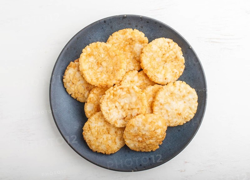 Traditional japanese rice chips cookies with honey and soy sauce on a blue ceramic plate on a white wooden background. Top view, flat lay, close up