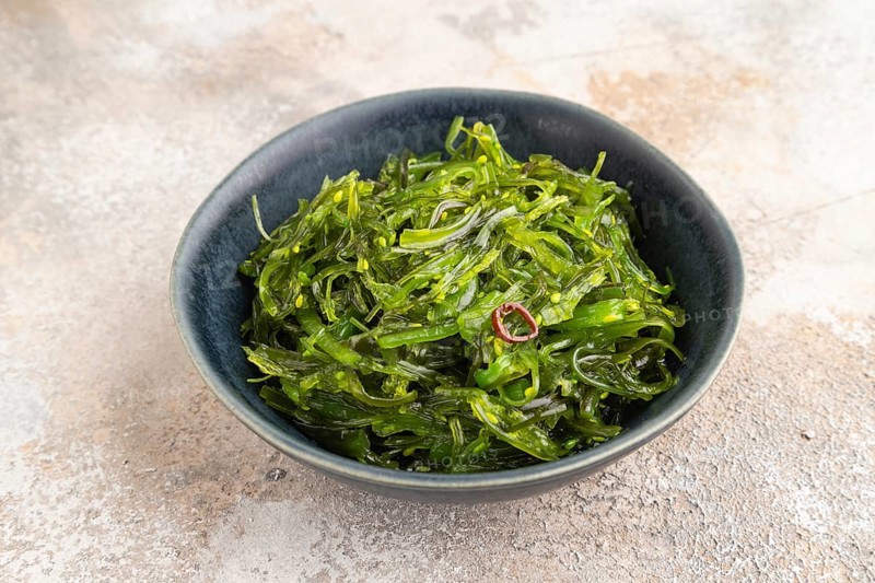 Chuka seaweed salad in blue ceramic bowl on brown concrete background. Side view, close up