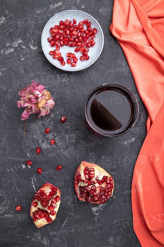 Glass of pomegranate juice on a black concrete background with red textile. Top view, close up, flat lay