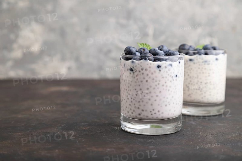 Yogurt with blueberry and chia in glass on black concrete background. Side view, close up, copy space