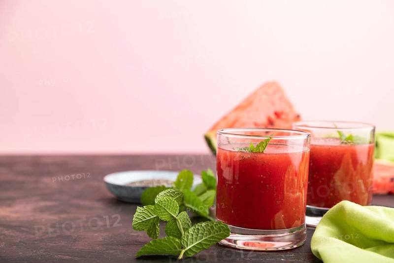 Watermelon juice with chia seeds and mint in glass on a black and pink background with green textile. Healthy drink concept. Side view, close up, selective focus, copy space