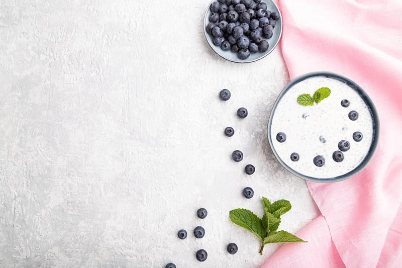 Yogurt with blueberry in ceramic bowl on gray concrete background and pink linen textile. top view, flat lay, copy space