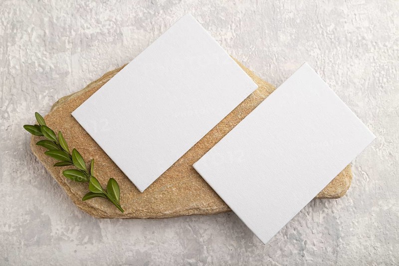 White paper business card, mockup with natural stone and boxwood branch on gray concrete background. Blank, flat lay, top view, still life, canvas, copy space