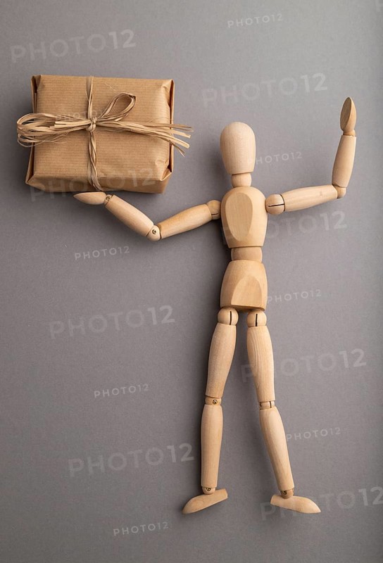 Wooden mannequin holding a gift box on gray pastel background. close up, isolated, delivery concept