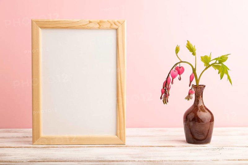 Wooden frame with pink dicentra, broken heart in ceramic vase on pink pastel background. side view, copy space, mockup, template, spring, summer minimalism concept