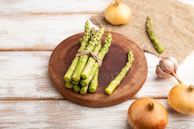 Bunch of fresh green asparagus, garlic, onion on white wooden background. Side view, close up. harvest, healthy, vegan food, concept