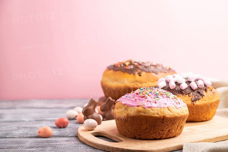 Homemade glazed and decorated easter pies with chocolate eggs and rabbits on a gray and pink background and linen textile. Side view, selective focus, copy space