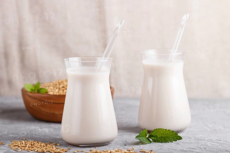 Organic non dairy oats milk in glass and wooden plate with oats seeds on a gray concrete background. Vegan healthy food concept, close up, side view