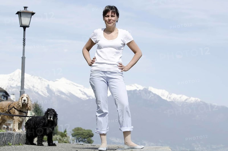 Proud and Elegant Woman Standing with Her Cute Dogs and Snow Capped Mountain in a Sunny Day in Brissago, Ticino, Switzerland, Europe