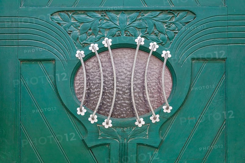 Close-up of a green door with elaborate decorations and a small oval glass window with a metal grille, Blankenburg, Saxony-Anhalt, Germany, Europe