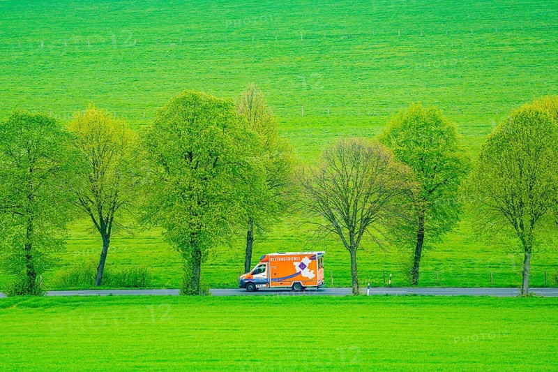 Ambulance on a country road, green fields, meadows, trees line the 2-lane road, spring, near Schwelm, North Rhine-Westphalia, Germany, Europe