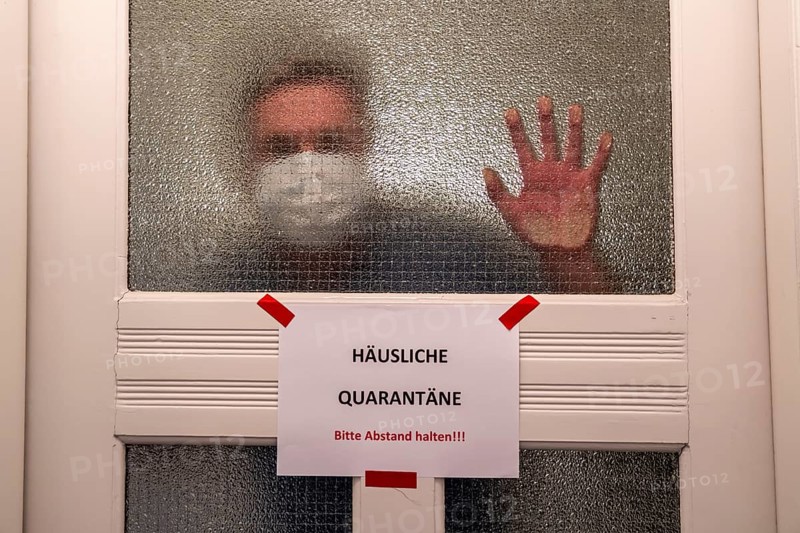 Symbolic image Domestic quarantine, man is in isolation at home due to a suspected corona infection, warning sign for visitors on the front door, communicating with a visitor through the door