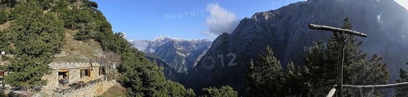 Mountain hut nestled in a wooded mountain landscape with views of snow-capped peaks under a blue sky, entrance to the Samaria Gorge, Omalos Plateau, Lefka Ori, White Mountains, mountain massif, west, Crete, Greece, Europe