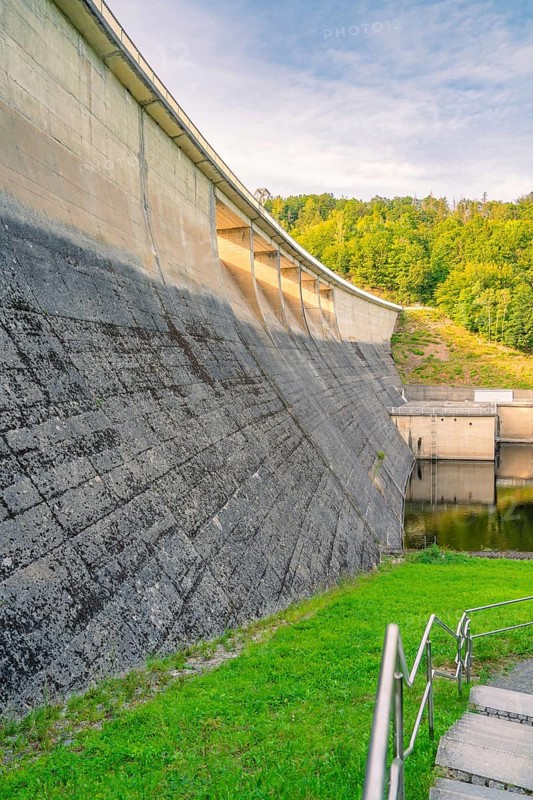Concrete dam surrounded by green grass and lush forest in the background in sunny weather, Rappbodetalsperre, Harz Mountains, Germany, Europe