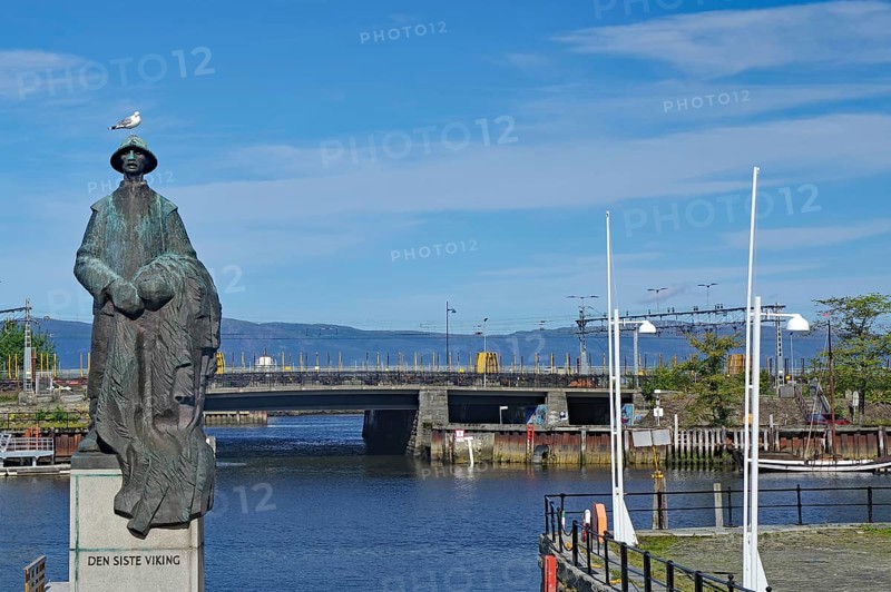 Statue of a fisherman in front of a river and a bridge under a blue sky, the last Viking, Nidarelva, Trondheim, Tröndelag, Norway, Europe
