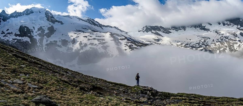Mountaineer on a rock in front of a mountain landscape, high fog in the valley, panorama with glaciated mountains, summit Großer Möseler and Furtschaglkees, Berliner Höhenweg, Zillertal Alps, Tyrol, Austria, Europe