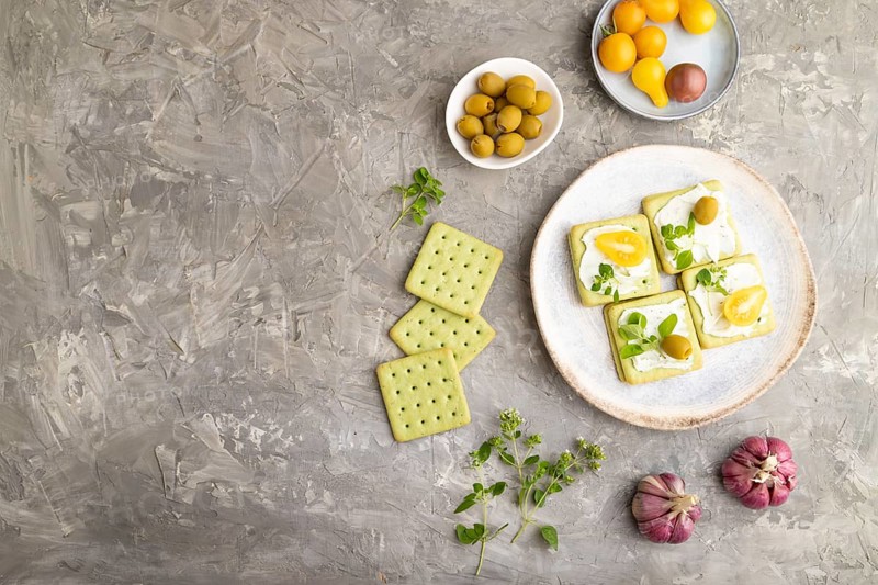 Green cracker sandwiches with cream cheese and cherry tomatoes on gray concrete background. top view, flat lay, copy space