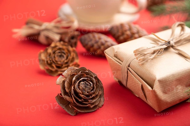 Christmas or New Year composition. Decorations, box, cinnamon, cones, fir and spruce branches, cup of coffee, on a red paper background. Side view, close up, selective focus
