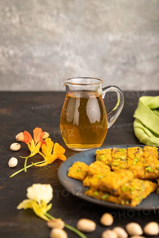 Traditional iranian dessert sohan with glass of green tea on a black concrete background and green textile. side view, close up, selective focus