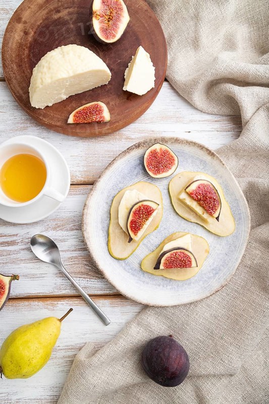 Summer appetizer with pear, cottage cheese, figs and honey on a white wooden background and linen textile. Top view, flat lay, close up