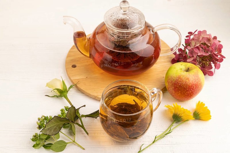 Red tea with herbs in glass teapot on white wooden background. Healthy drink concept. Top view, close up