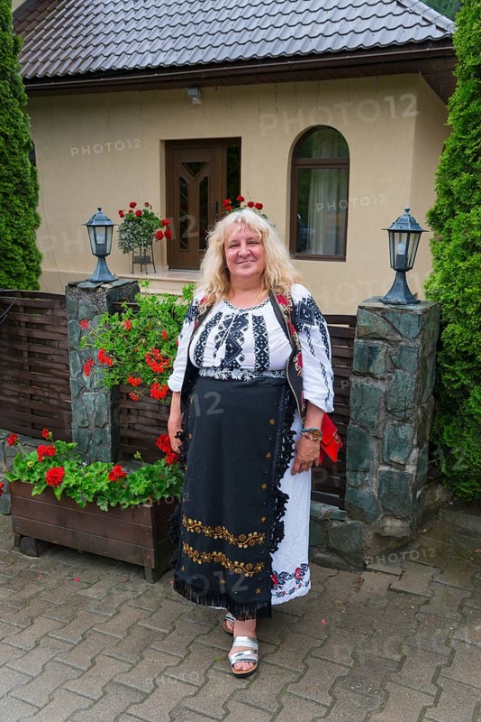 Woman in traditional outfit smiling in front of a house with flowers, Woman in traditional traditional costume, Vadu Motilor, Alba, Transylvania, Romania, Europe