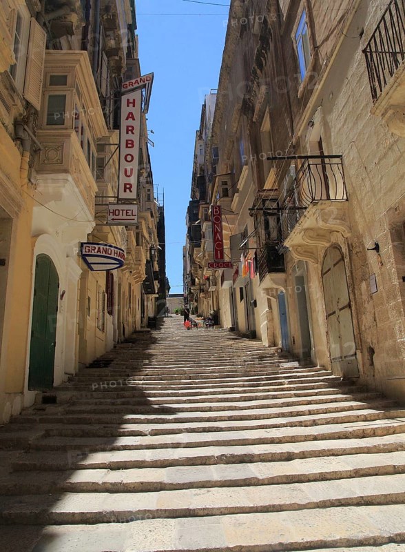 Steps climb hill of narrow street historic housing with traditional balconies in city centre of Valletta, Malta, Europe