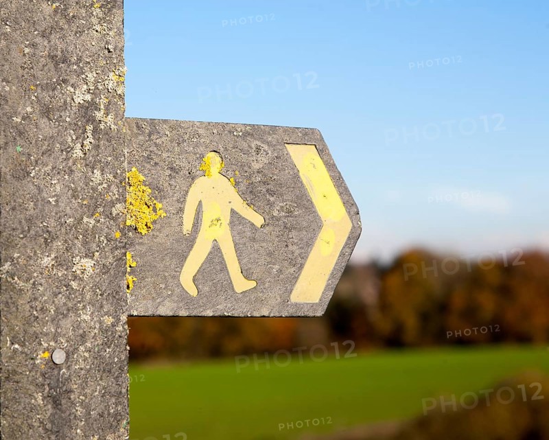 Close up of footpath sign with yellow human figure walking and direction arrow pointing the way, Wiltshire, England, UK
