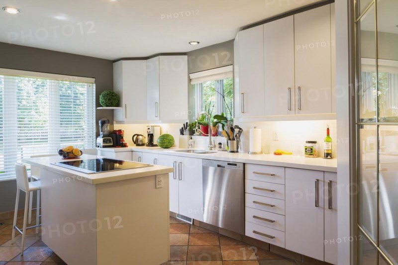 White cabinets, quartz countertop and island with glass cooktop and high back bar stool in kitchen inside a luxurious residential home, Quebec, Canada, North America