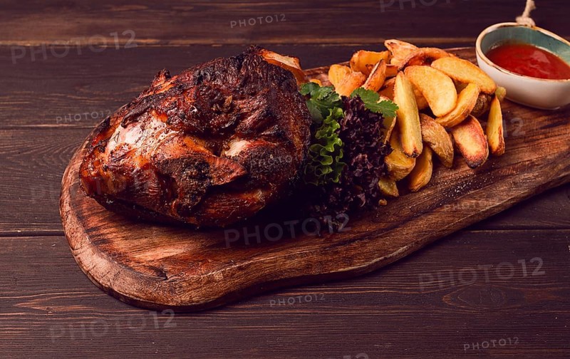 Pork knuckle, in soy-honey sauce, with fried potatoes, on a wooden chopping board, homemade, no people