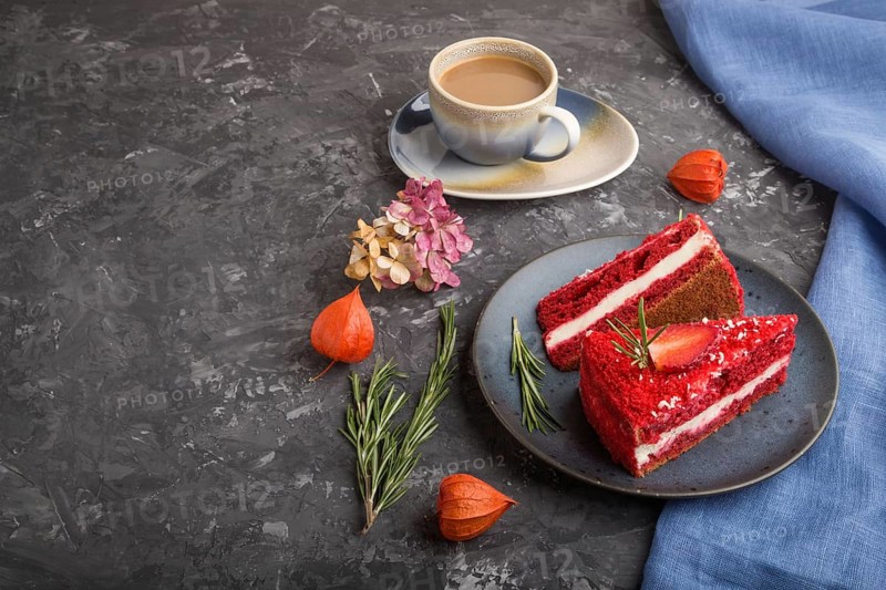 Homemade red velvet cake with milk cream and strawberry with cup of coffee on a black concrete background with blue textile. side view, close up, copy space