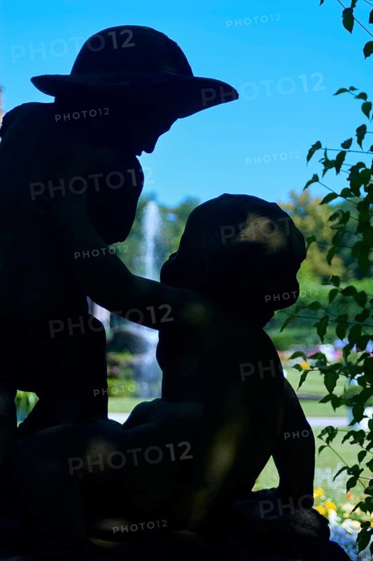 Two childlike figures, butens, angels, as a statue in the shade of a tree in front of a fountain in a park-like garden, Hofgarten Veitshöchheim, Veitshöchheim, Mainfranken, Bavaria, Germany, Europe
