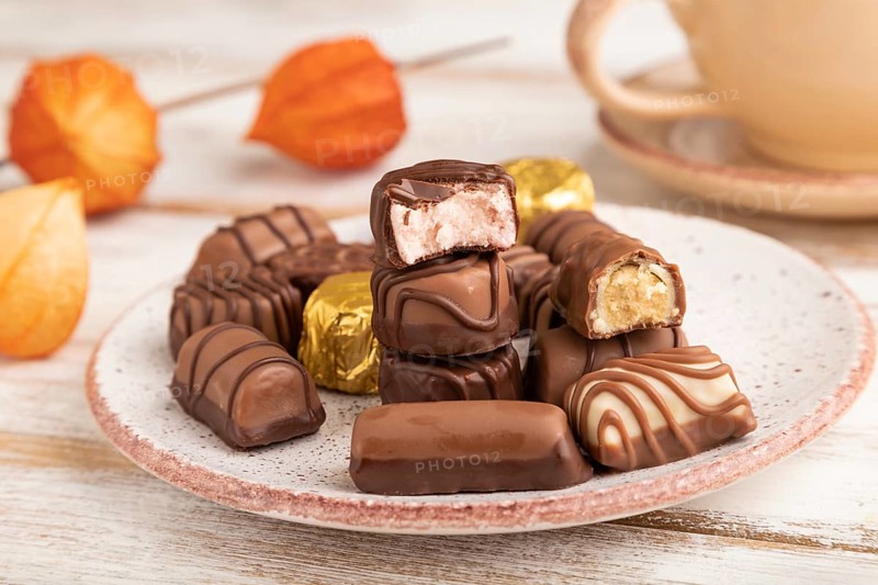 Chocolate candies with cup of coffee and physalis flowers on a white wooden background and orange textile. side view, close up, selective focus