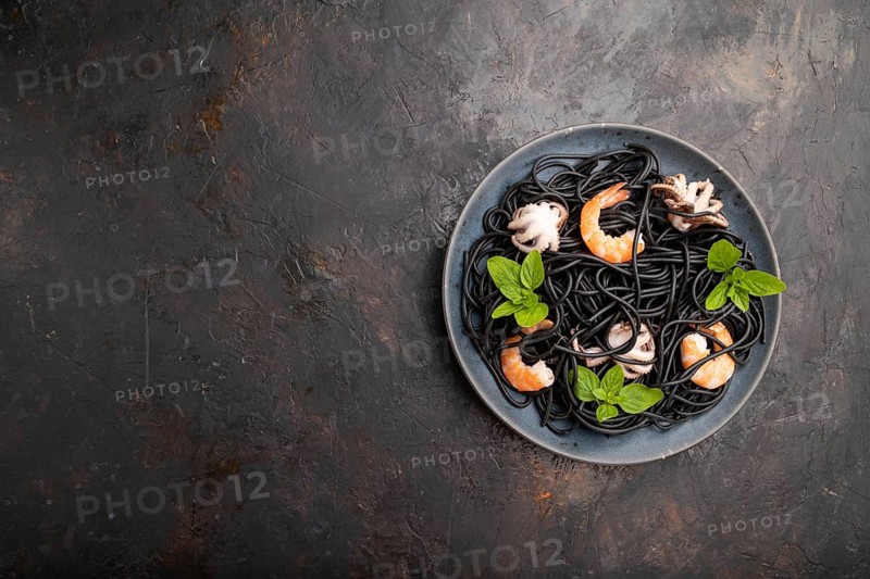 Black cuttlefish ink pasta with shrimps or prawns and small octopuses on black concrete background. Top view, flat lay, copy space