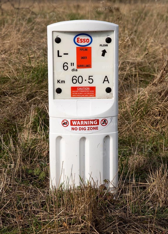 Close up of Esso gas pipeline under surveillance marker warning no dig zone, Salisbury Plain, Wiltshire, England, UK