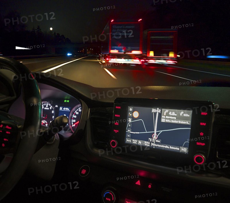 Night-time road scene with two lorries, in front an illuminated cockpit with sat nav of a car, Bavaria, Germany, Europe
