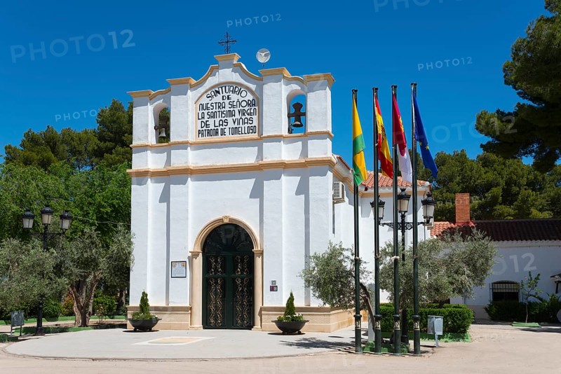 Historische Kapelle mit verschiedenen Fahnen und Bäumen unter blauem Himmel, Ermita y museo Virgen de las Viñas, Eremitage und Museum Virgen de las Viñas, Heiligtum Unserer Lieben Frau, der Heiligen Jungfrau der Reben, Tomelloso, Ciudad Real, Kastilien-La Mancha, Spanien