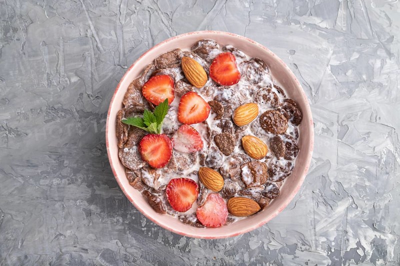 Chocolate cornflakes with milk, strawberry and almonds in ceramic bowl on gray concrete background. Top view, flat lay, close up