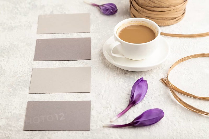 Gray paper business card mockup with spring snowdrop crocus flowers and cup of coffee on gray concrete background. Blank, business card, side view, copy space, still life. spring concept