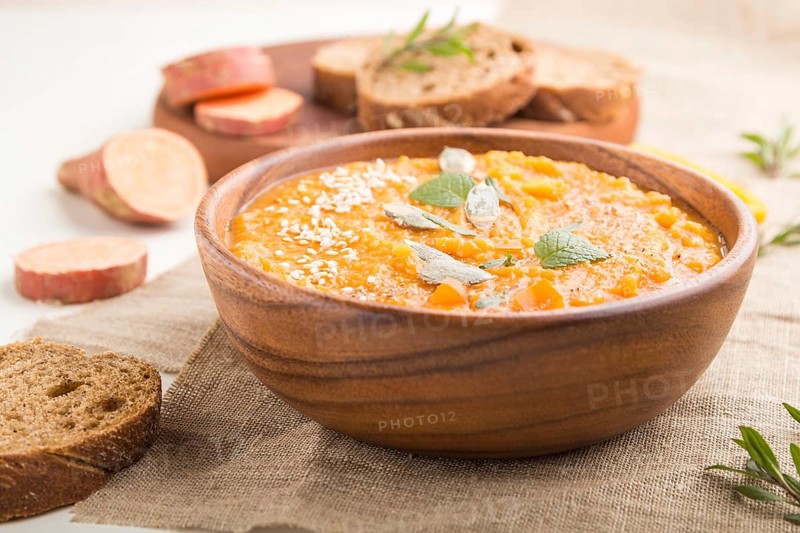 Sweet potato or batata cream soup with sesame seeds in a wooden bowl on a white wooden background with linen textile. side view, close up, selective focus